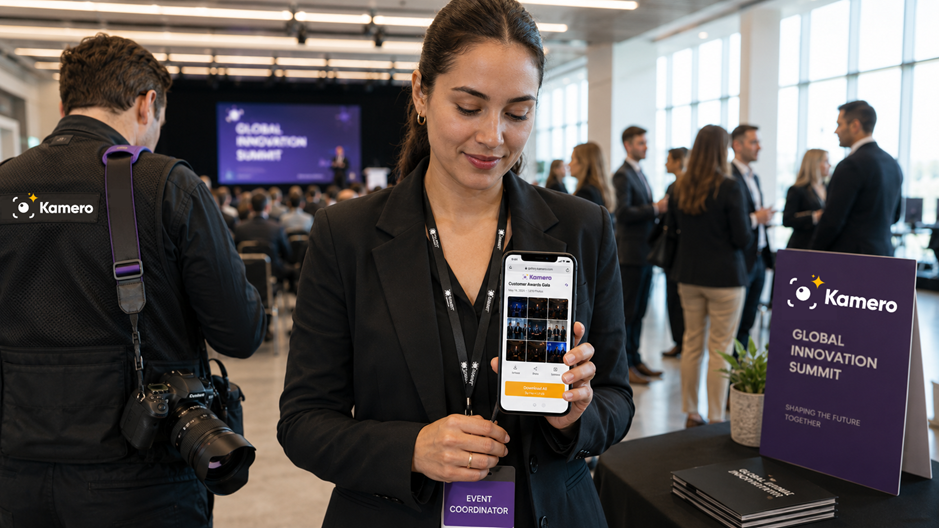 A female corporate event coordinator holding a smartphone that displays a live Kamero web gallery filled with real-time attendee photos at a business conference. She wears an event coordinator badge and stands near a purple Kamero-branded welcome sign reading "Global Innovation Summit", while an event photographer with a professional camera and a Kamero logo strap shoots the background audience, demonstrating instant camera-to-cloud photo delivery and guest engagement.