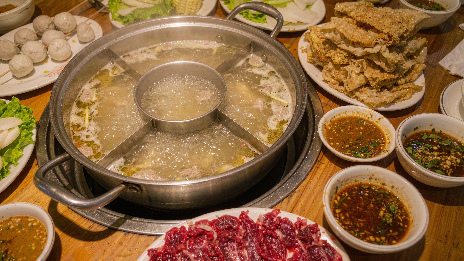 潮汕牛肉火锅桌上的鲜切牛肉、牛肉丸与蘸料,分隔锅底沸腾