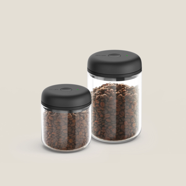 Fellow Atmos Vacuum Canister with black lid, filled with coffee beans on a white background.