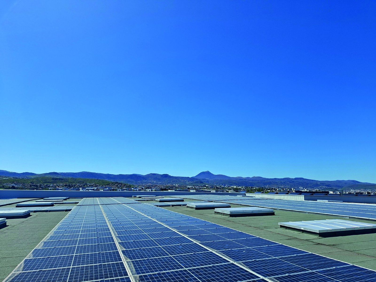 Centrale photovoltaïque en toiture réalisée par JR Énergie à Cournon-d'Auvergne, le puy de Dôme à l'horizon