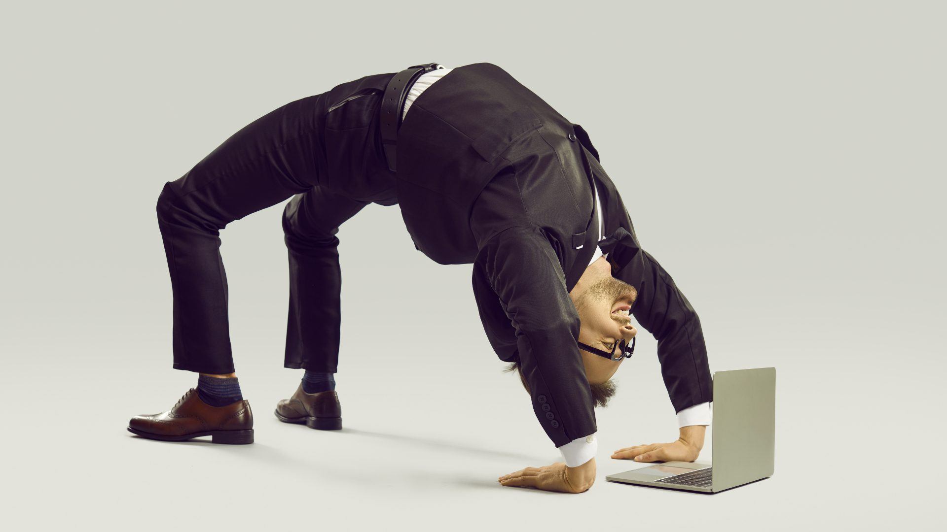 Happy energetic businessman practises yoga positions while working on laptop computer.
