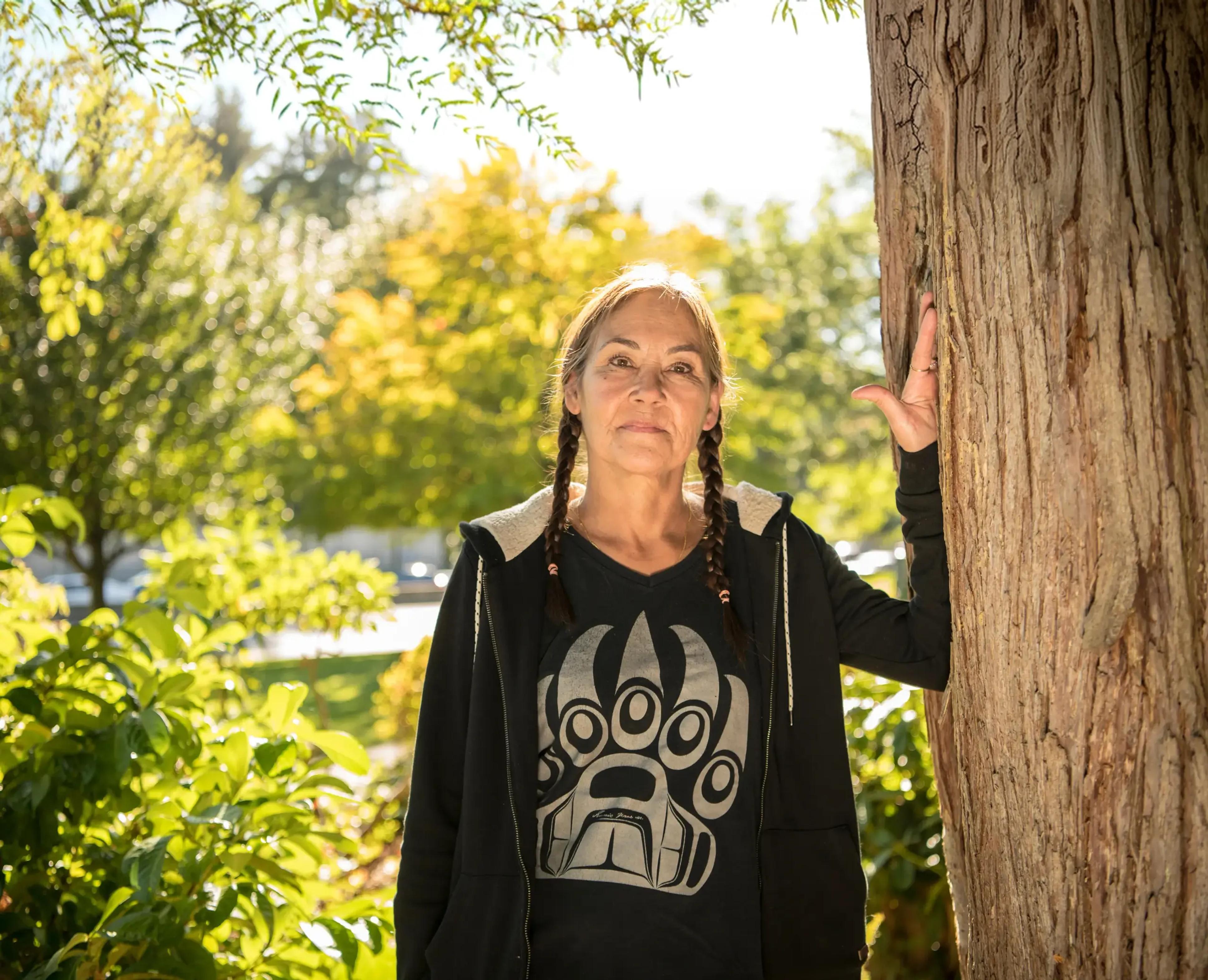 A person outdoors with their hands resting near a tree.