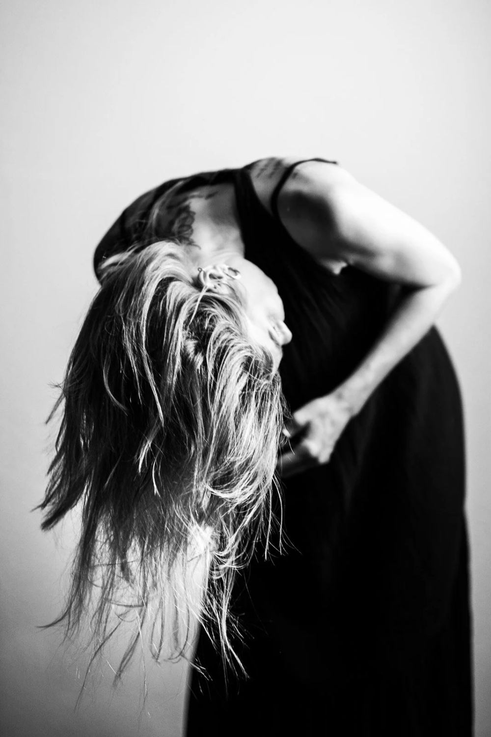Black-and-white studio portrait of a woman bending sideways with her hair hanging down