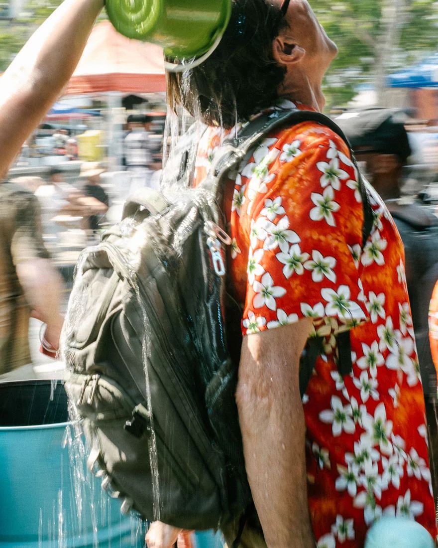 Man in a red floral shirt has a green bucket of water poured over his head