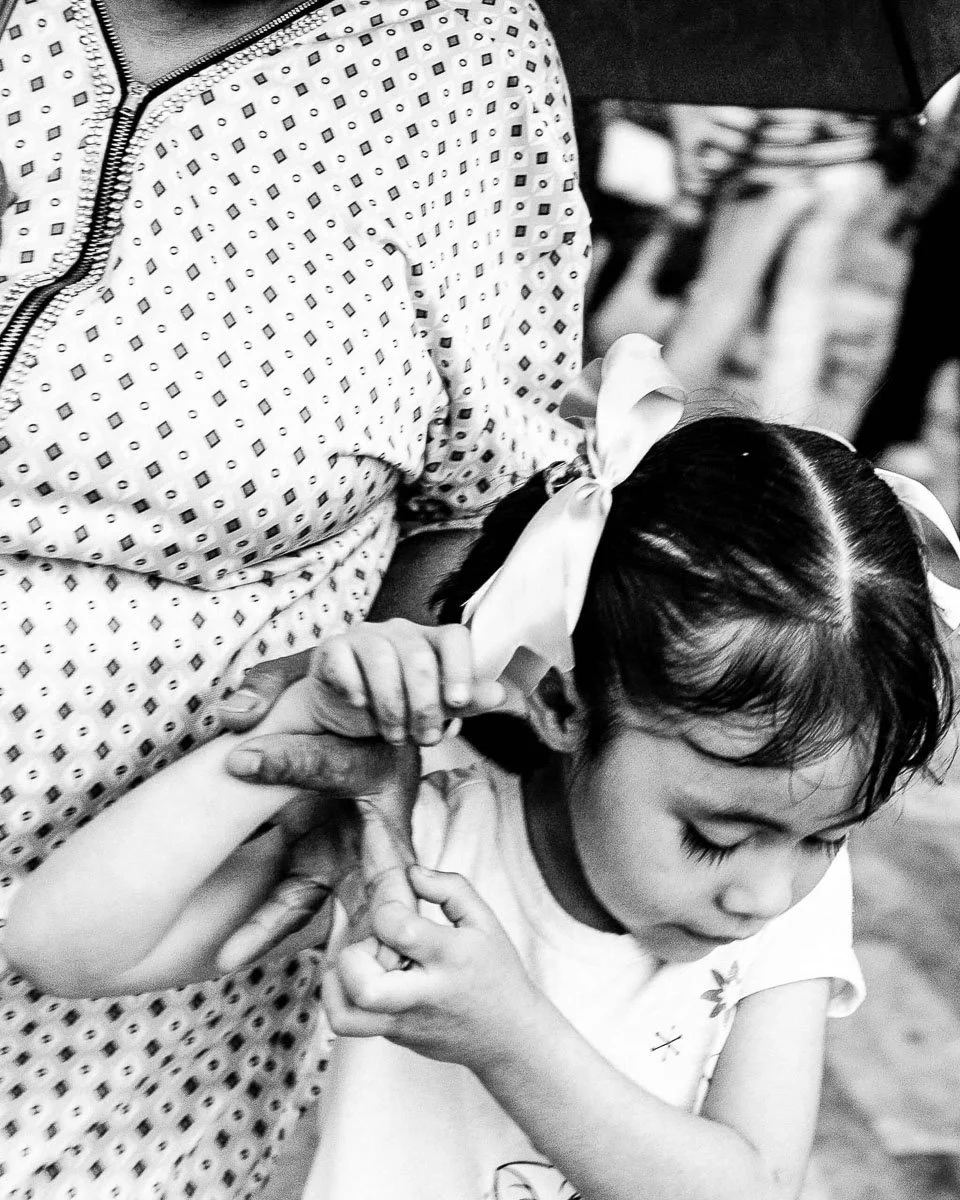 Black-and-white candid photograph of a young girl holding an adult's arm