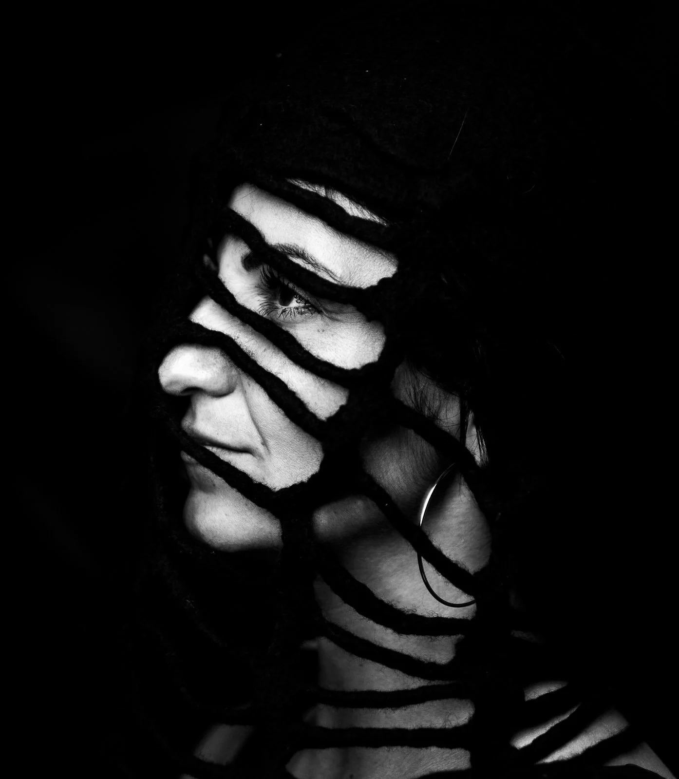 Studio portrait of a woman's face crossed by narrow bands of light and shadow