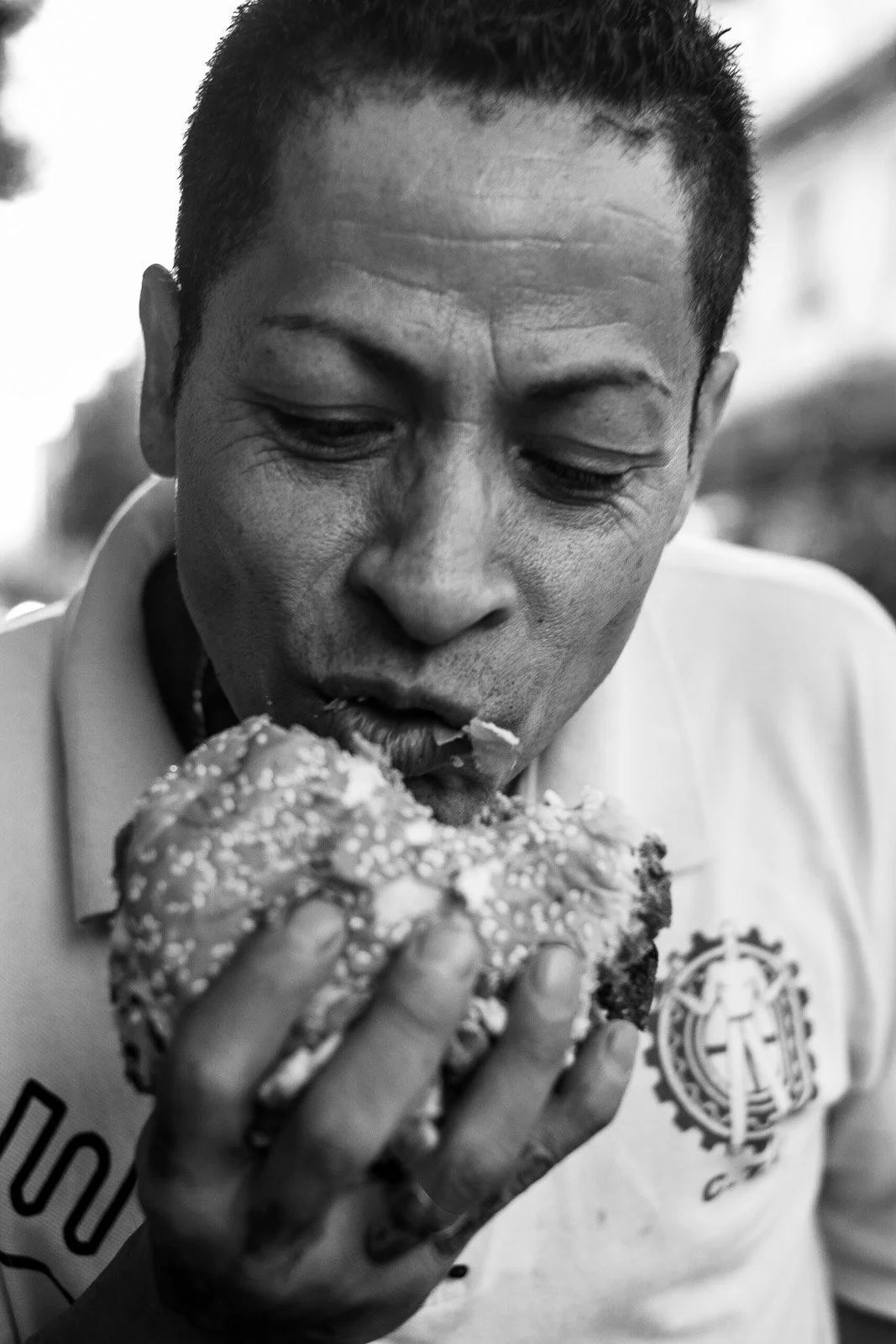 Close-up black-and-white photograph of a man taking a bite from a burger