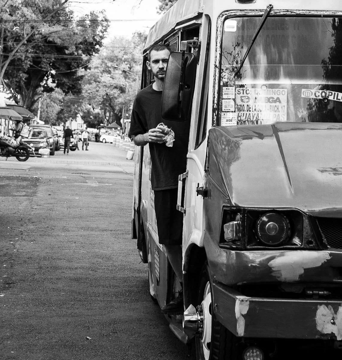 Black-and-white photograph of a man eating beside a small street vehicle