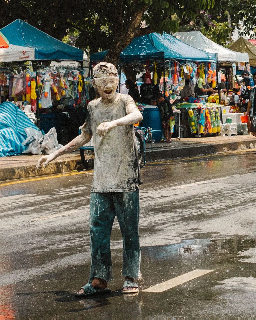 Man covered in white paste stands on a wet Chiang Mai street during Songkran