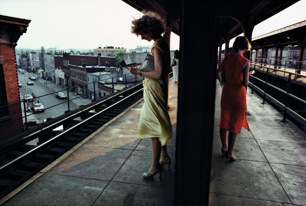 Two women stand on opposite sides of a column on an elevated subway platform, photographed by Bruce Davidson