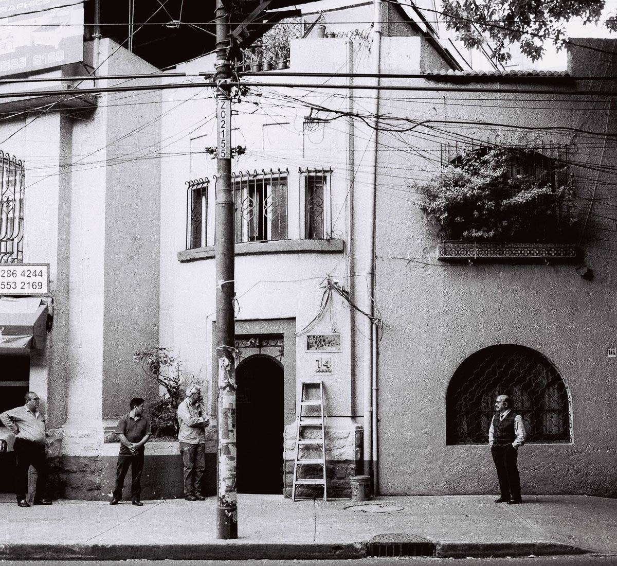Black-and-white film street photograph of men waiting beside a ladder in Mexico City.