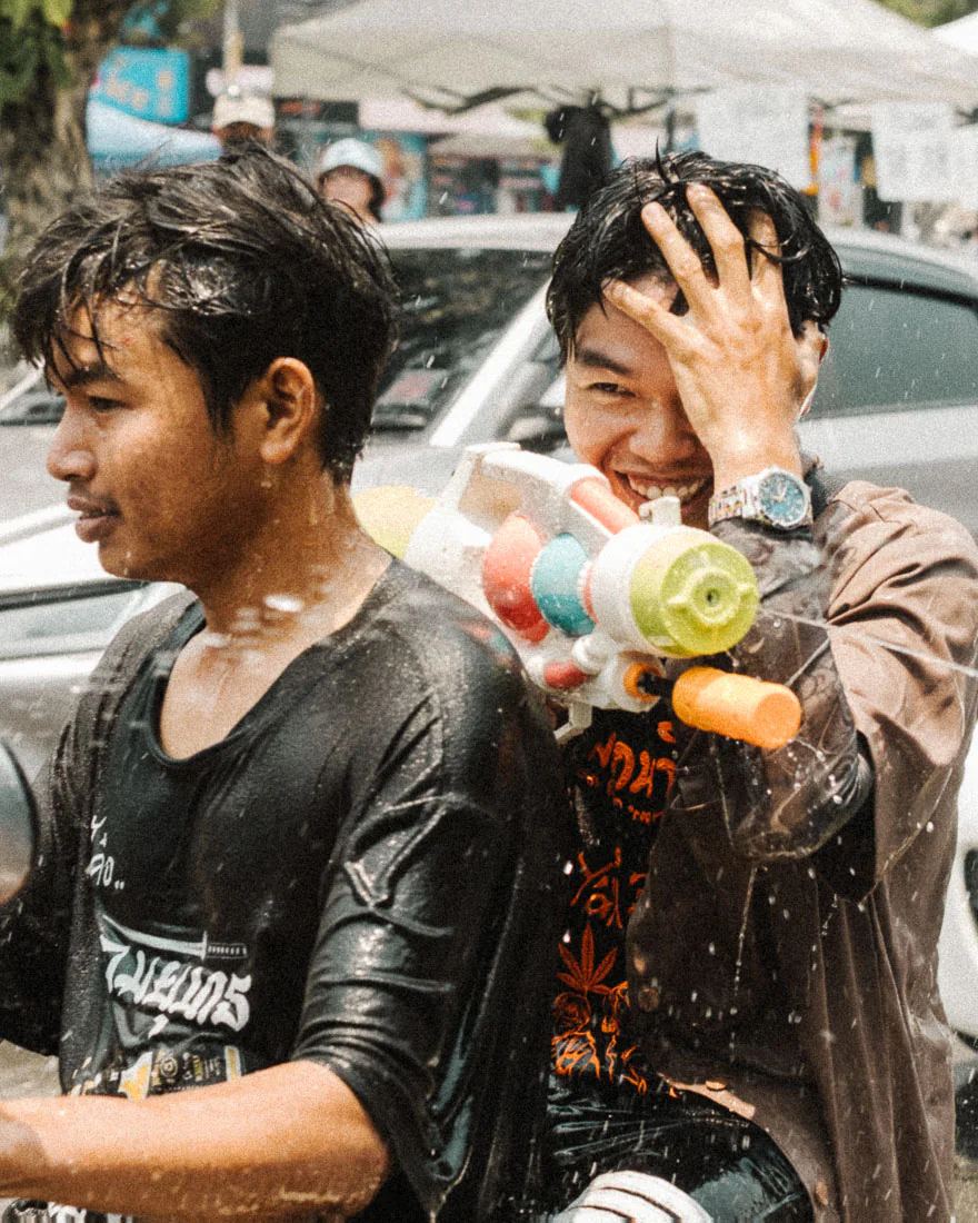 Smiling motorbike passenger holds a water gun behind a soaked rider