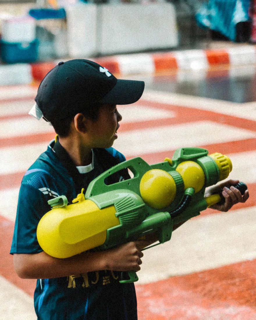 Boy carries an oversized green and yellow water gun during Songkran
