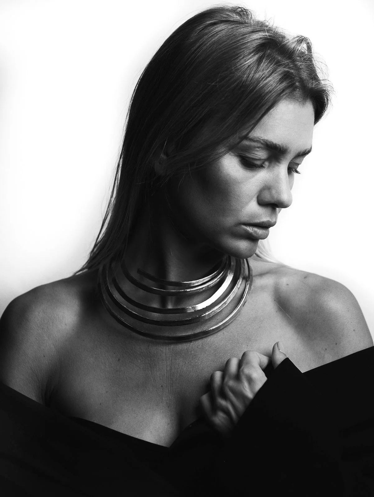 Black-and-white studio portrait of a woman looking down while wearing layered necklaces