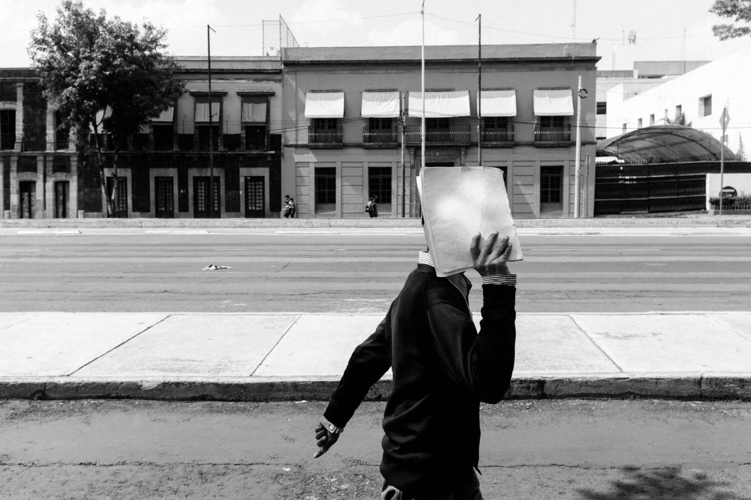 Black-and-white street photograph of a person shielding their face with a white bag