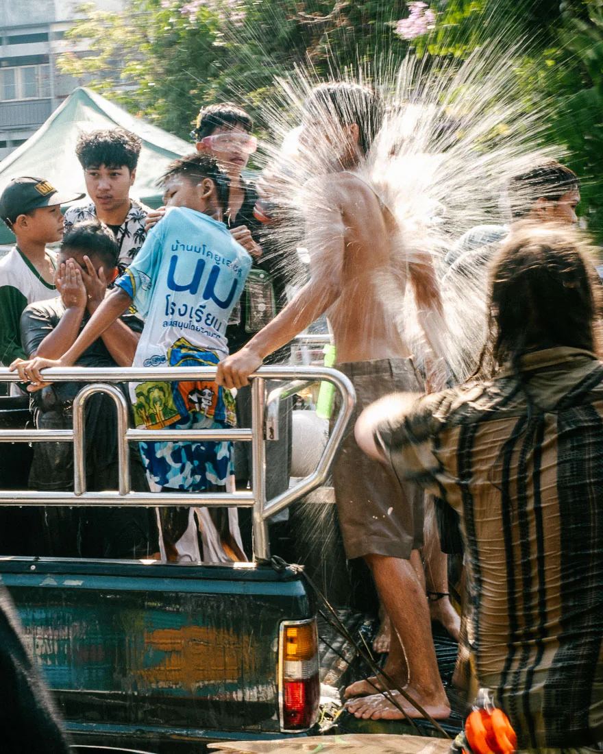 People standing in a pickup truck are hit by a burst of water during Songkran