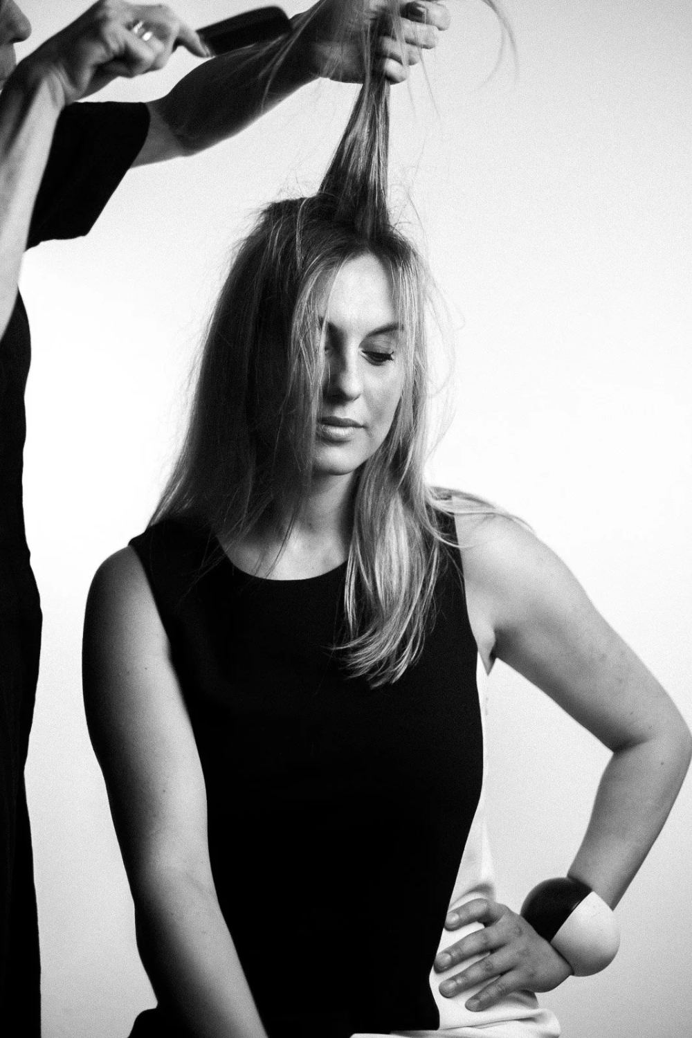 Black-and-white studio portrait of a woman as another person lifts a strand of her hair