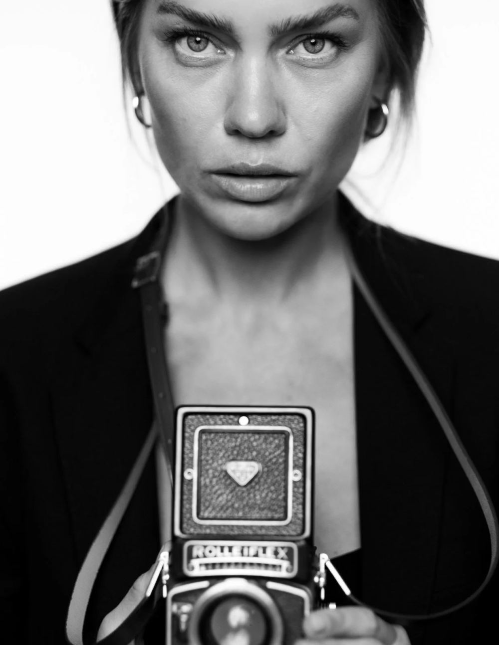 Black-and-white studio portrait of a woman holding a twin-lens reflex camera