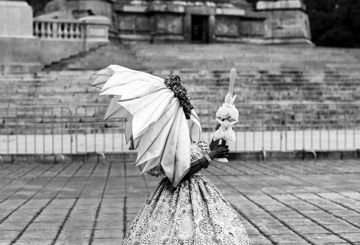 Day of the Dead participant in a patterned dress holding a parasol and a small skeleton figure