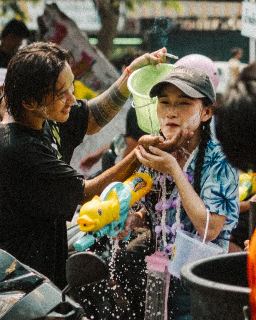 Man tips a green bucket over a woman holding a pig-shaped water gun