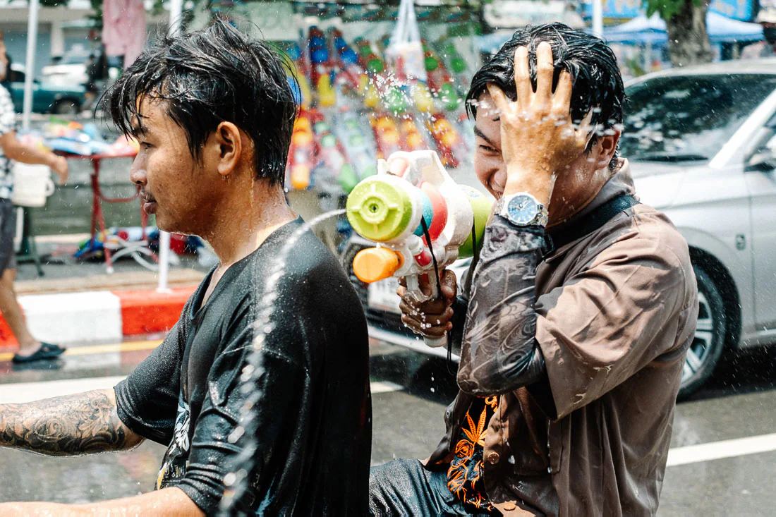 Motorbike passenger grips a water gun as two soaked men ride through Songkran