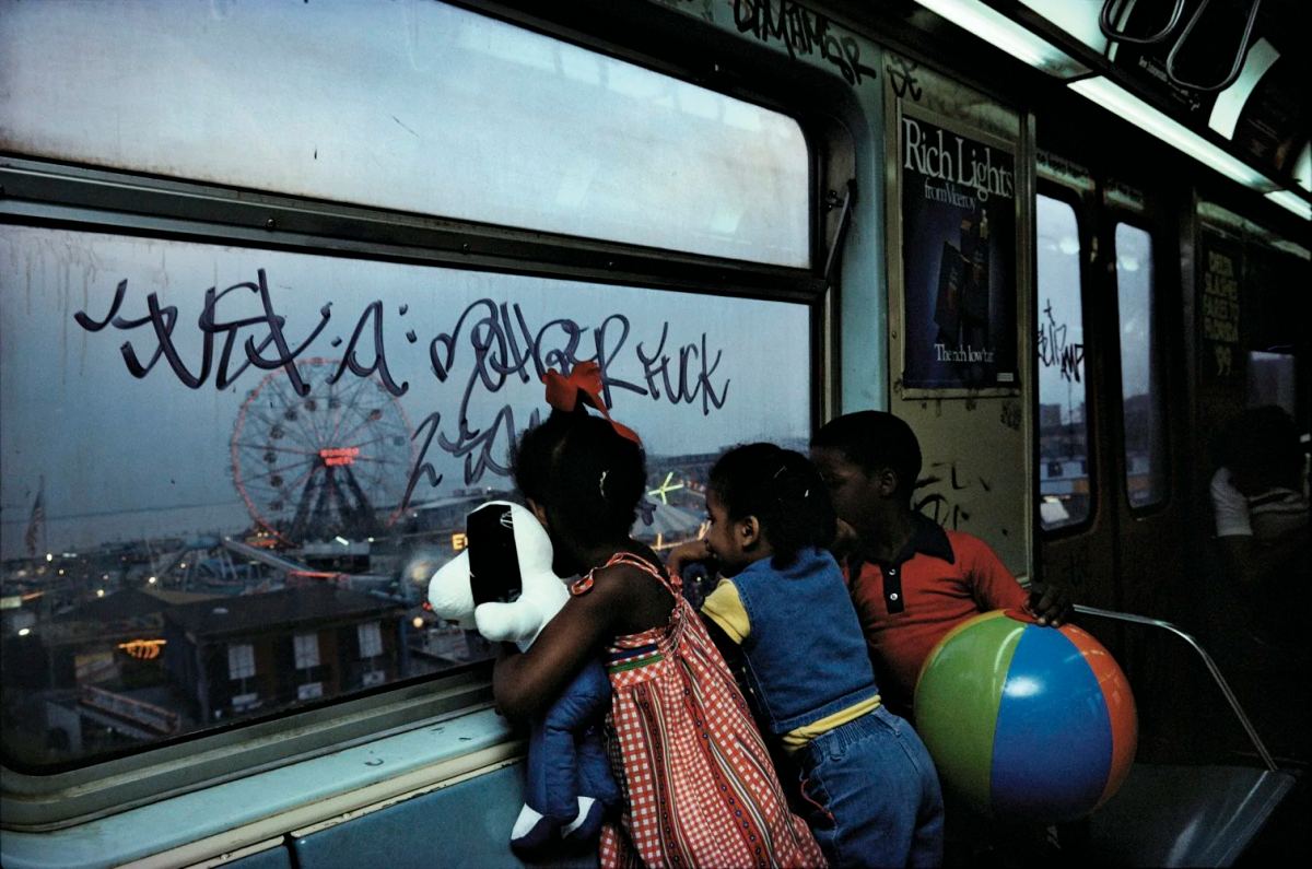 Children carrying a beach ball and toy look through a graffiti-covered subway window, photographed by Bruce Davidson