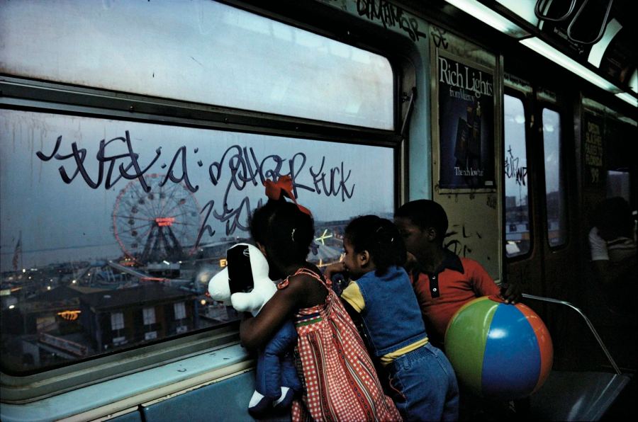 Children carrying a beach ball and toy look through a graffiti-covered subway window, photographed by Bruce Davidson