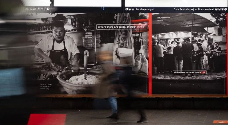 A passerby moves in front of Coca-Cola taco-stand campaign photographs in a subway station