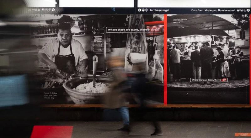 A passerby moves in front of Coca-Cola taco-stand campaign photographs in a subway station