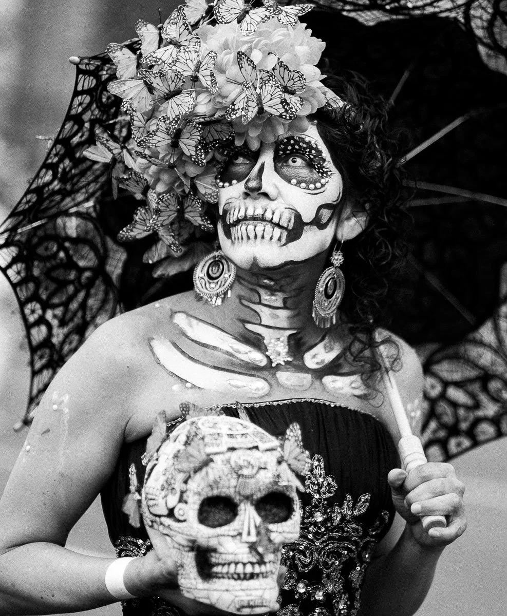 Day of the Dead participant with skull face paint and a flower crown holding a decorated skull