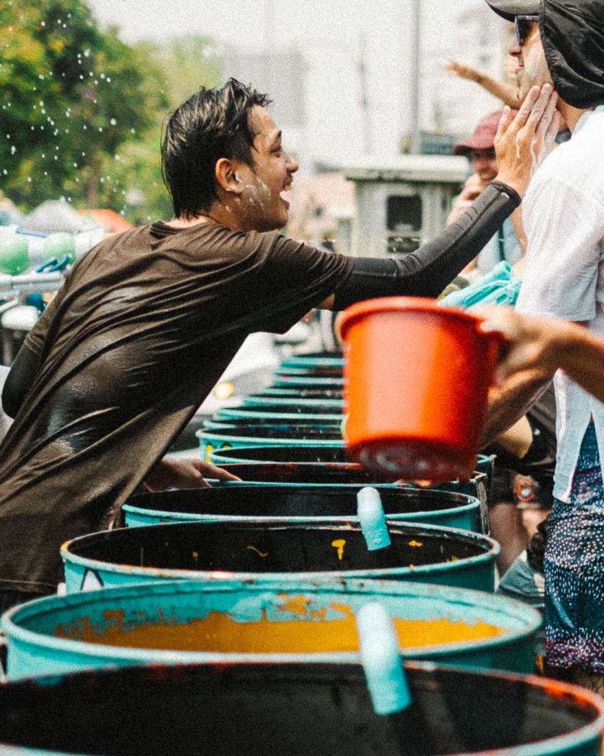 Man reaches across water barrels to apply white paste to another participant