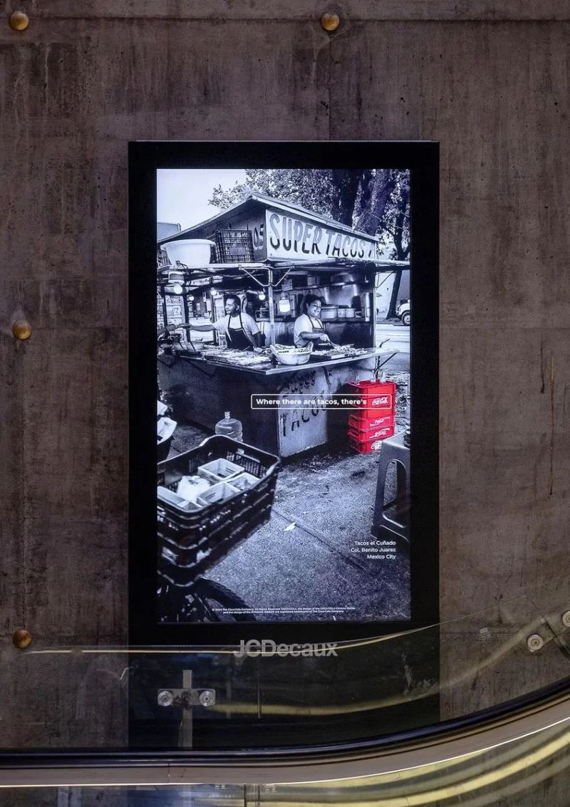 Coca-Cola taco-stand campaign photograph on a vertical display beside an escalator