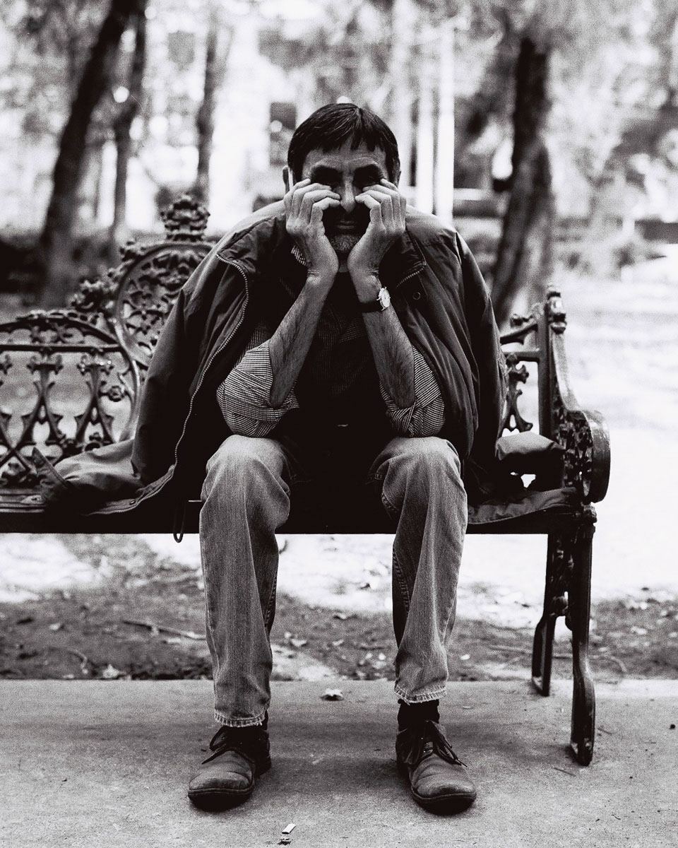 Black-and-white street portrait on film of a man seated on an ornate bench.