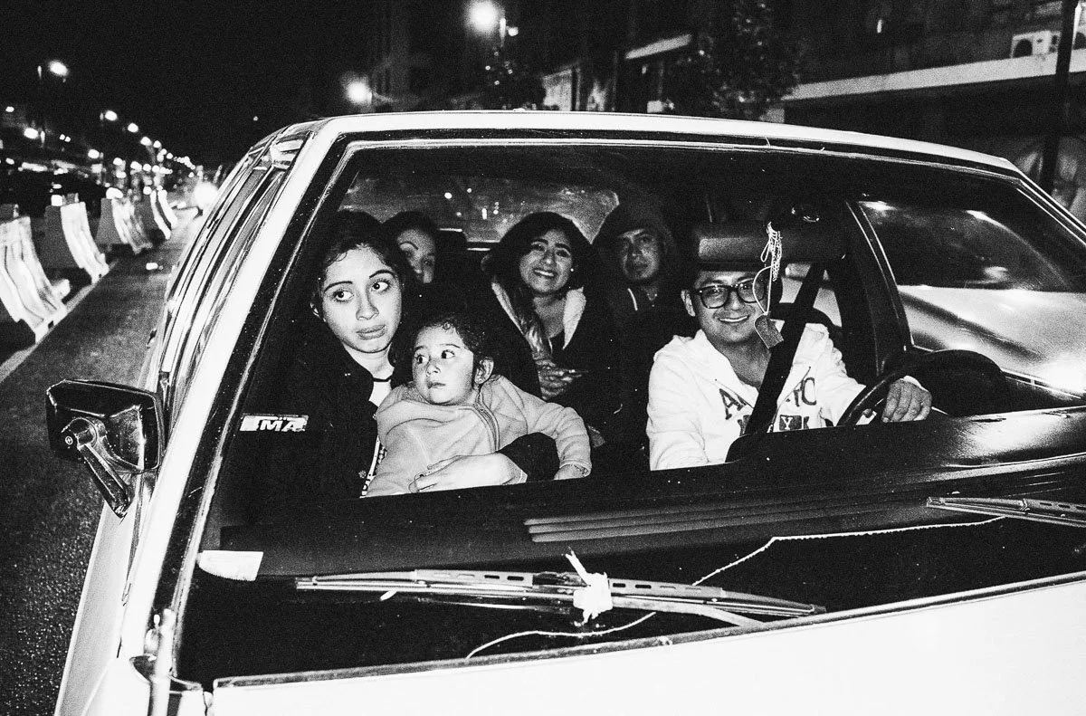 Black-and-white nighttime photograph of a family seen through a car windscreen
