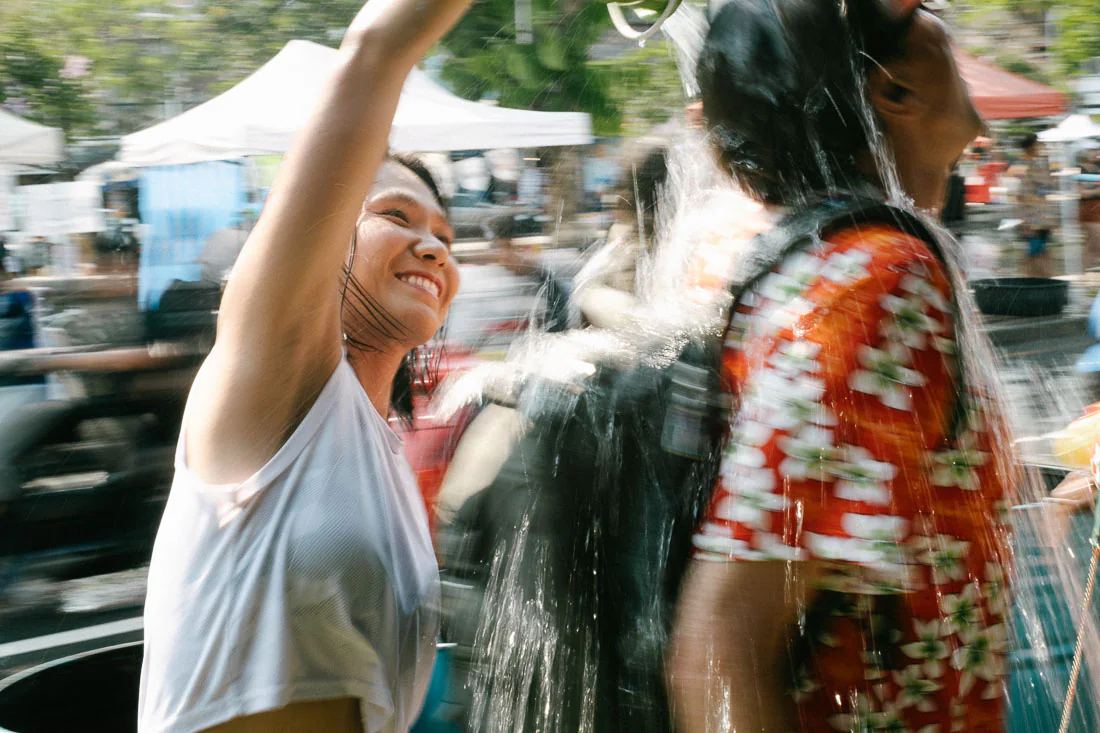 Smiling woman pours water over a man in a red floral shirt during Songkran