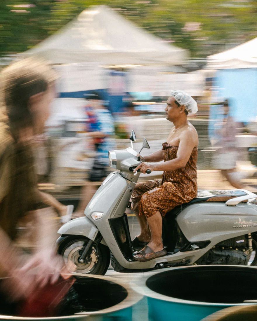 Scooter rider in a shower cap and floral dress passes through the Songkran crowd