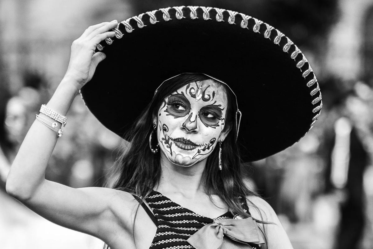 Day of the Dead participant with skull face paint holding the brim of a large sombrero