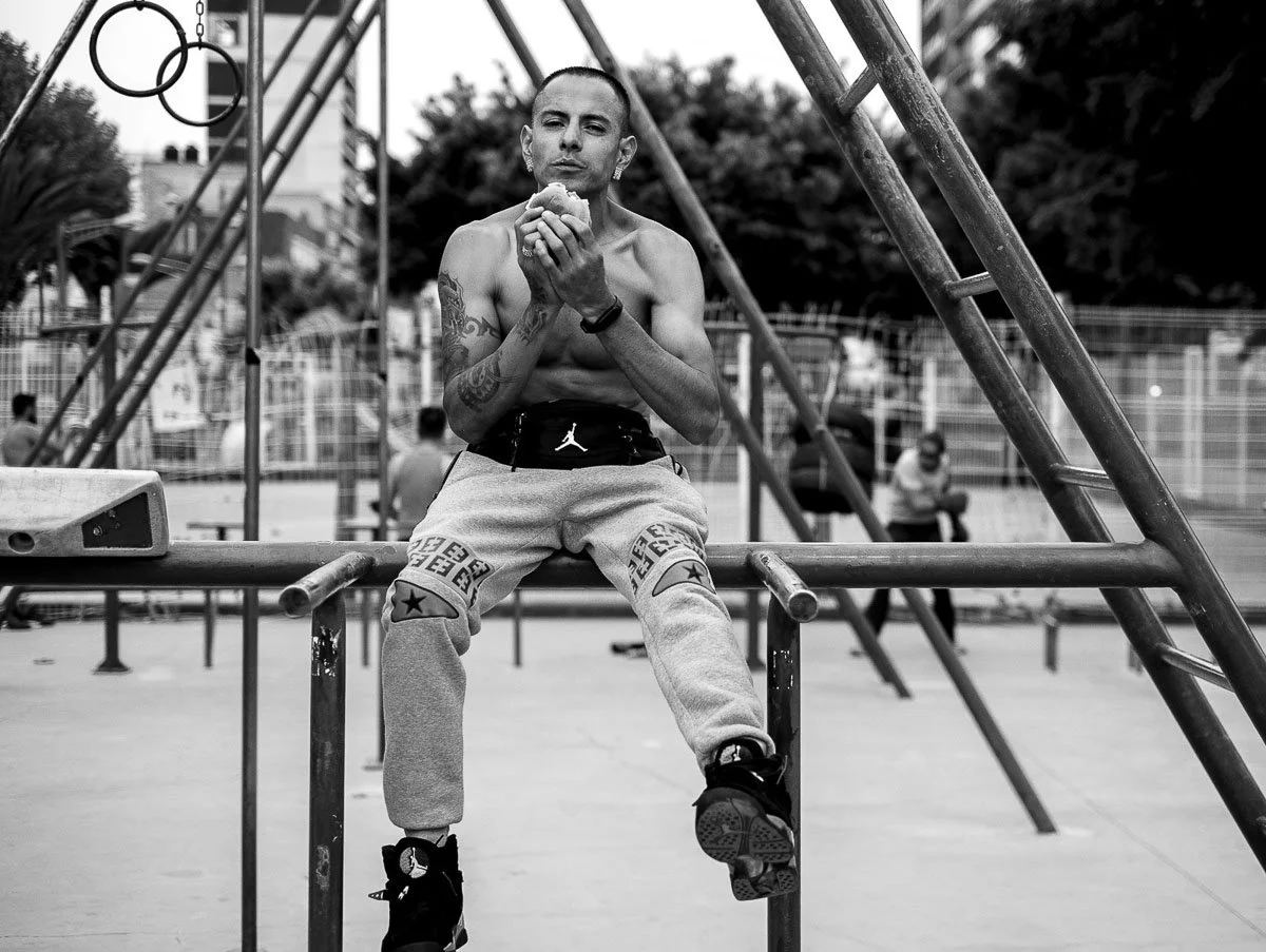Black-and-white photograph of a man eating a burger on outdoor exercise bars