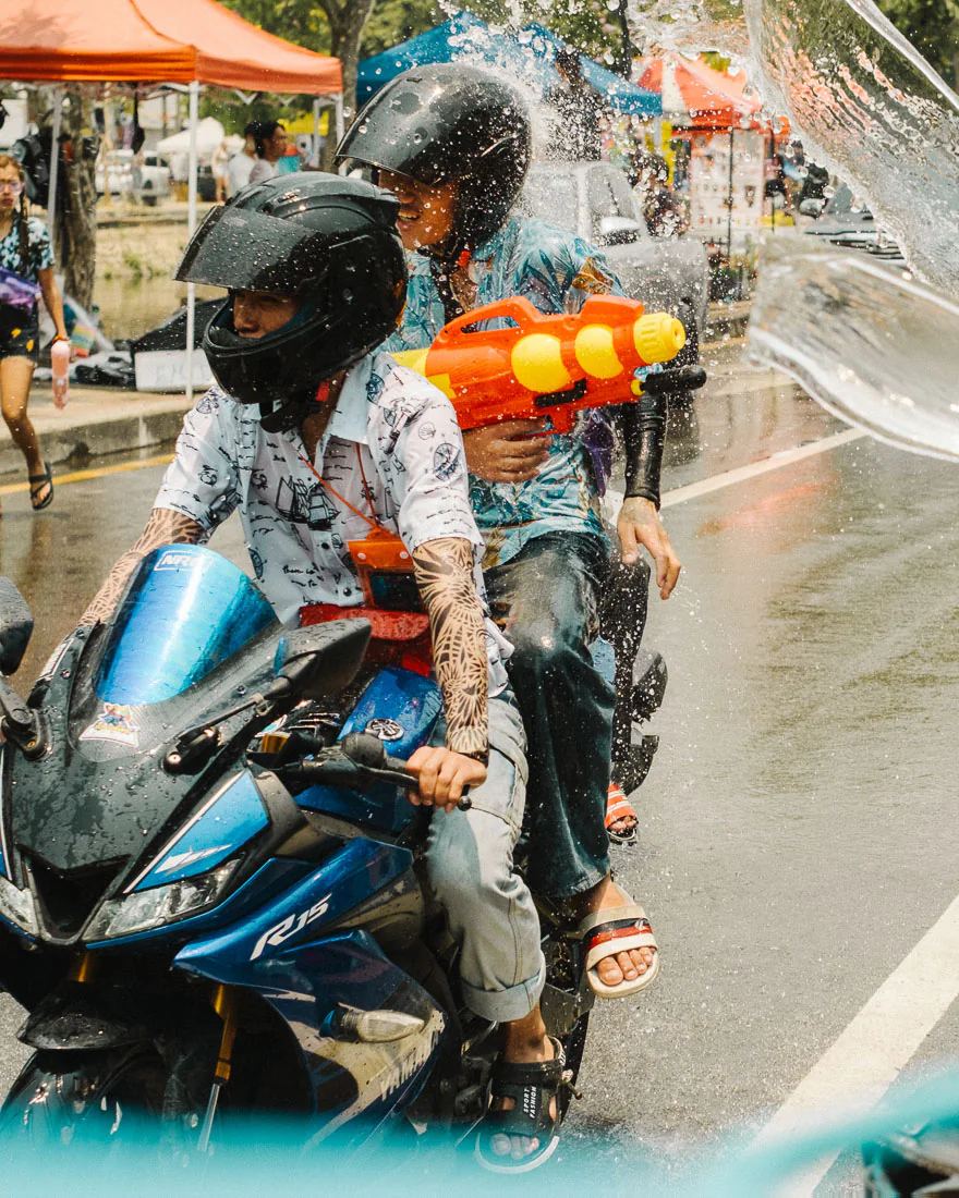 Motorbike passenger holding an orange water gun rides through a sheet of water