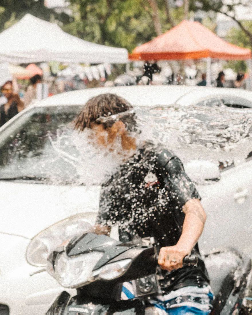 Scooter rider is struck in the face by a splash of water during Songkran