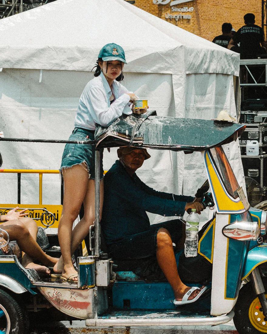 Woman stands on the back of a tuk-tuk holding a metal cup during Songkran