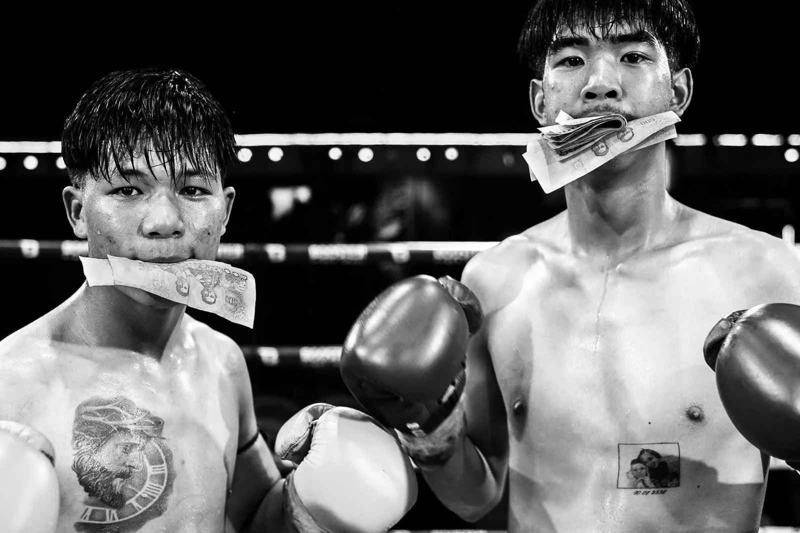 Two Muay Thai fighters pose with prize money between their teeth