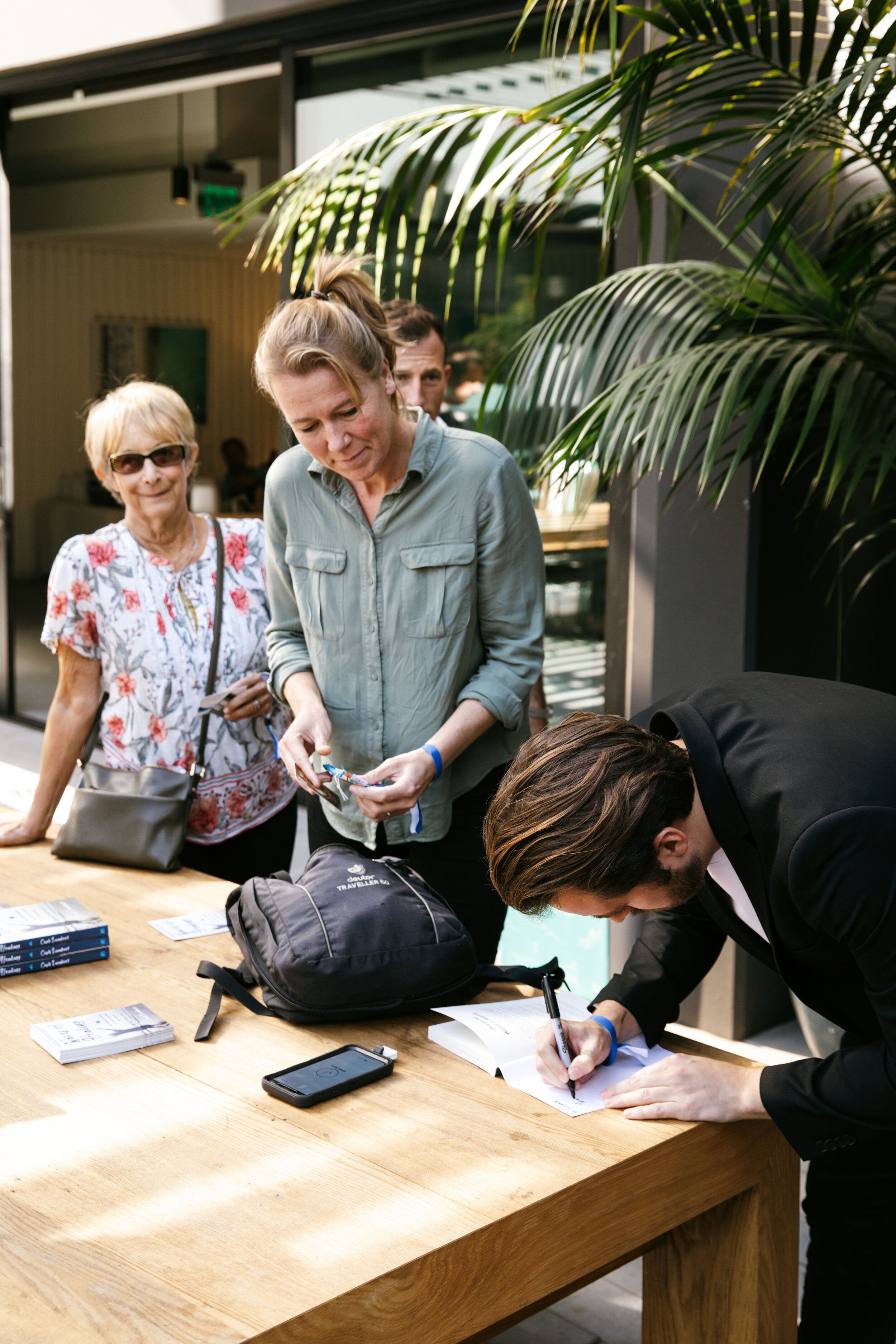 Cash Lambert signing a book at a table while two women look on