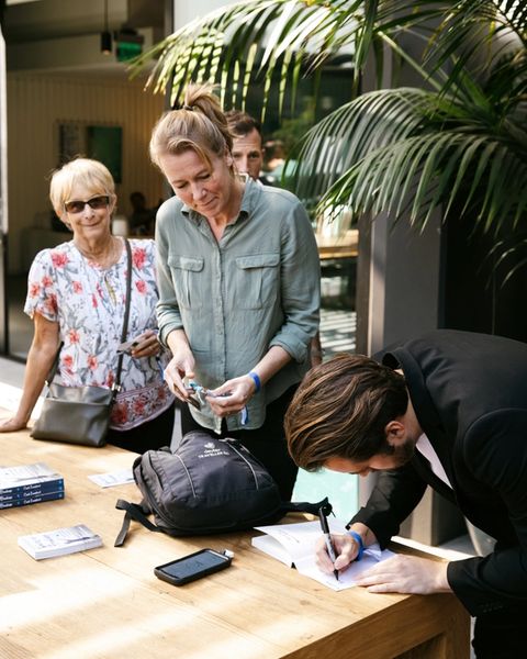 Cash Lambert signing a book at a table while two women look on