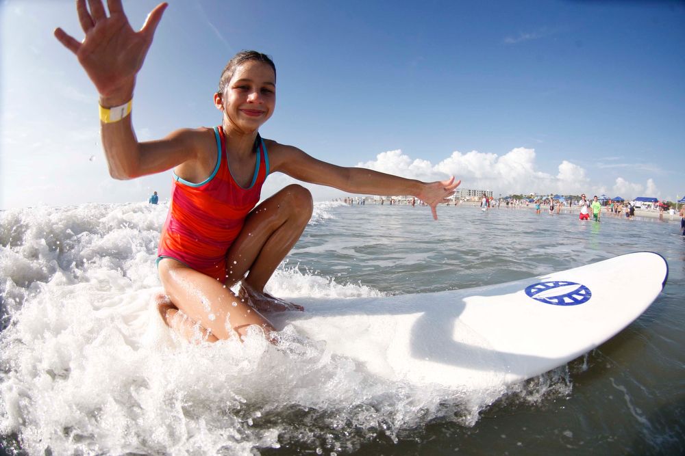 A girl kneeling on a surfboard in the waves, arms raised and waving
