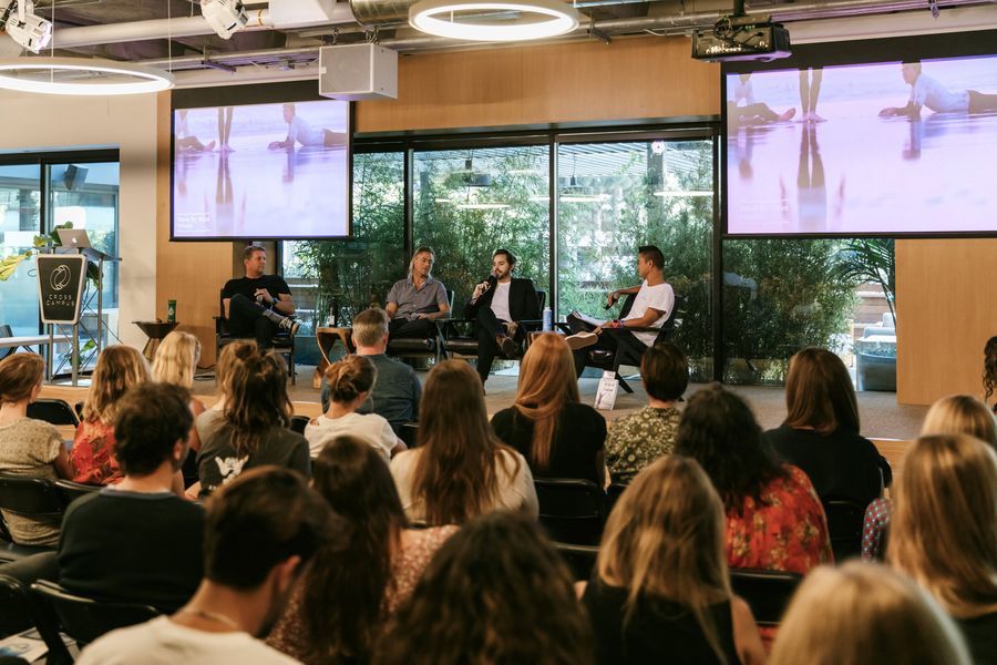 Wide view of a four-person panel discussion on stage with video screens above, seen from the audience