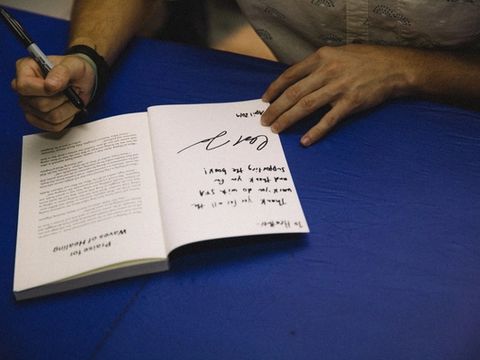 Close-up of hands signing a copy of Waves of Healing on a blue tablecloth