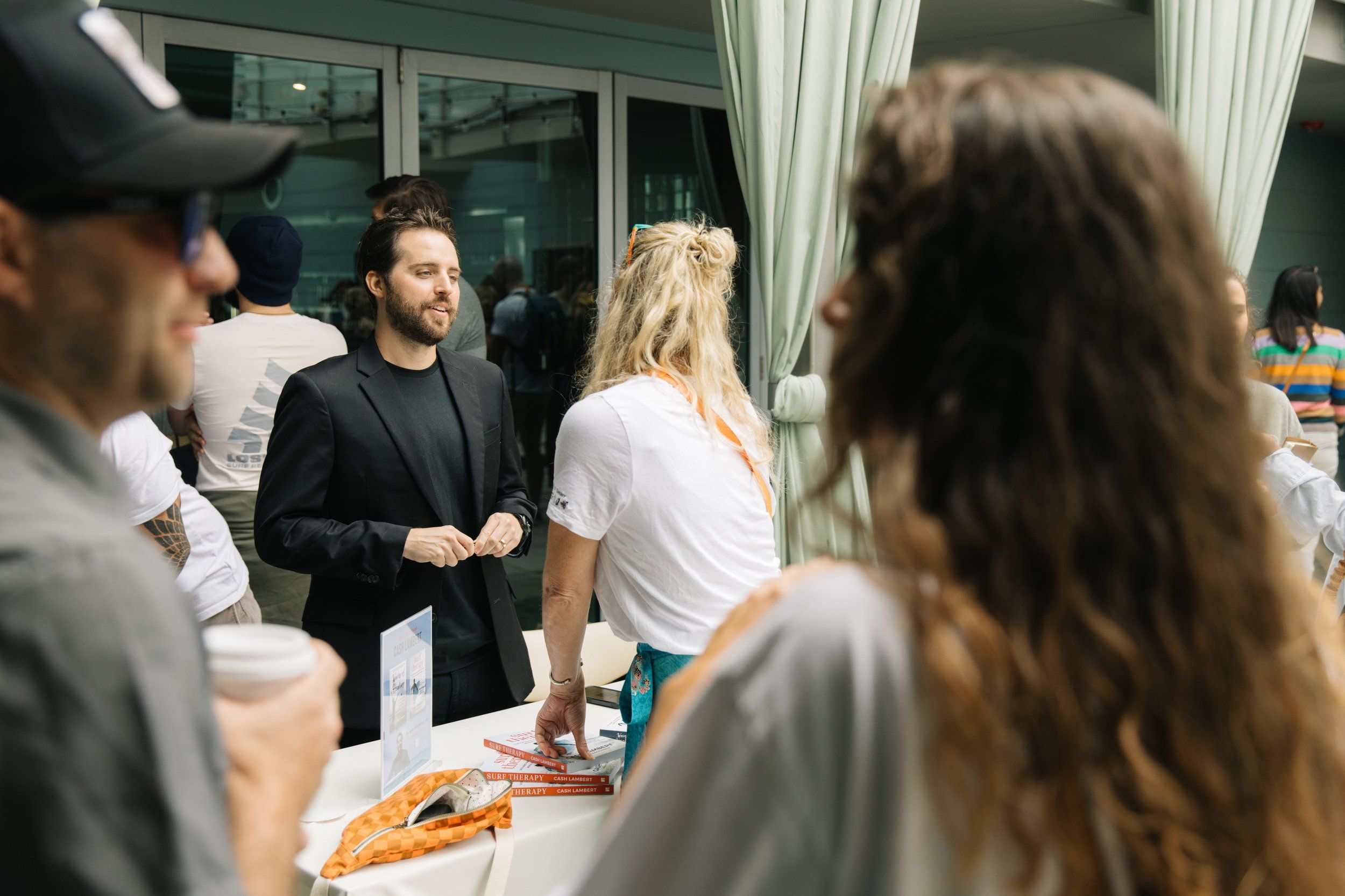 Cash Lambert talking with a woman at a table stacked with books, at an event