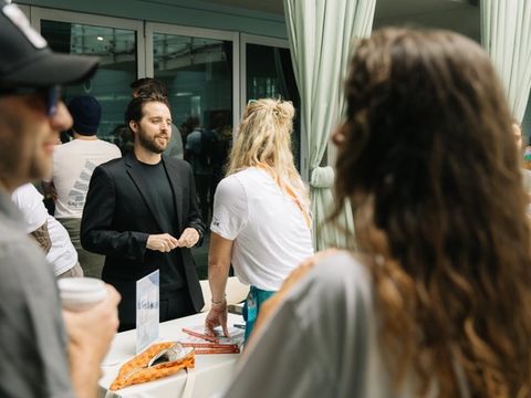Cash Lambert talking with a woman at a table stacked with books, at an event