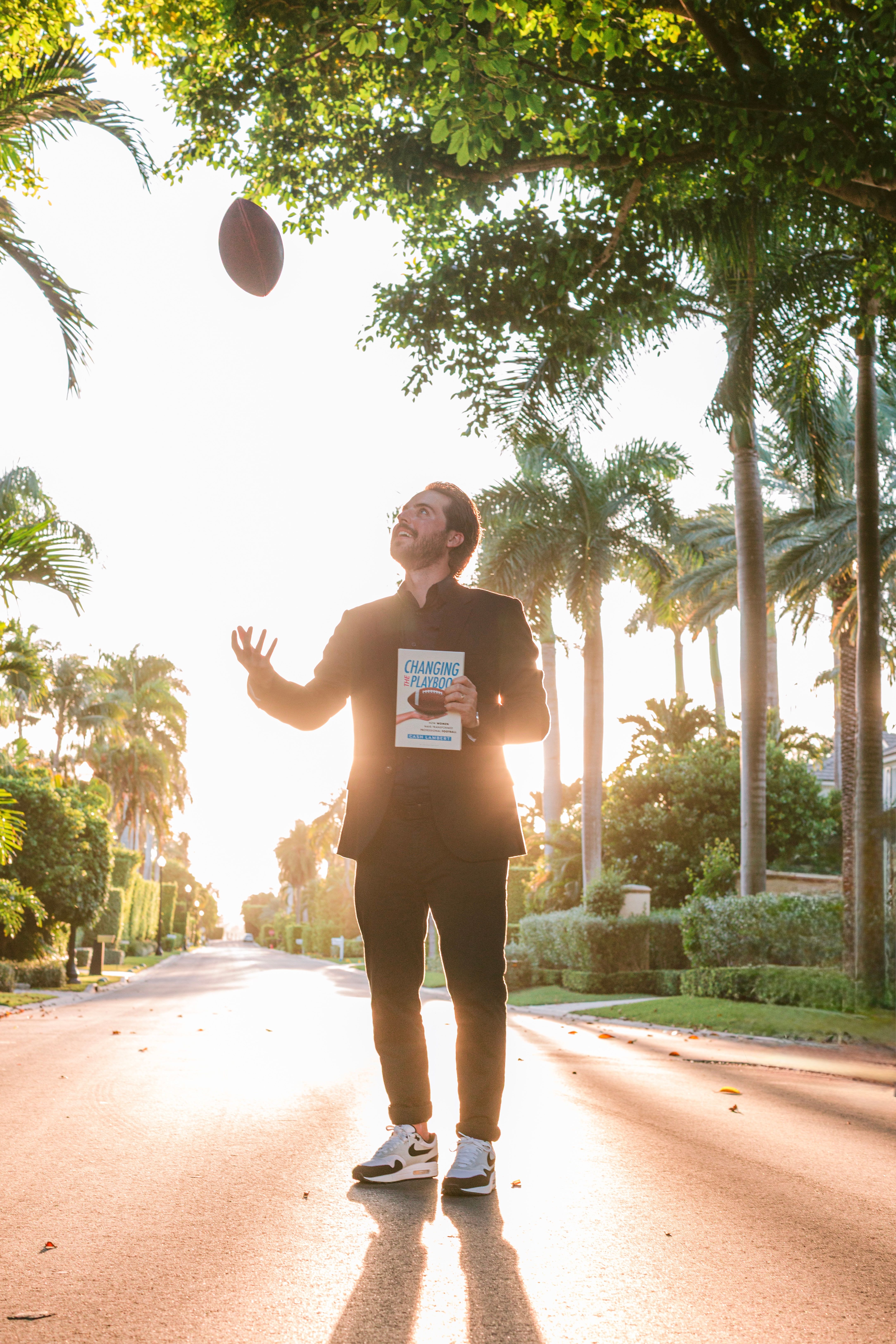 Cash Lambert on a palm-lined street, tossing a football and holding a copy of Changing the Playbook